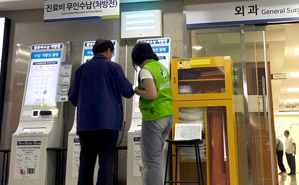 병원 무인 수납기 앞에서 봉사자가 어르신을 도와드리는 모습